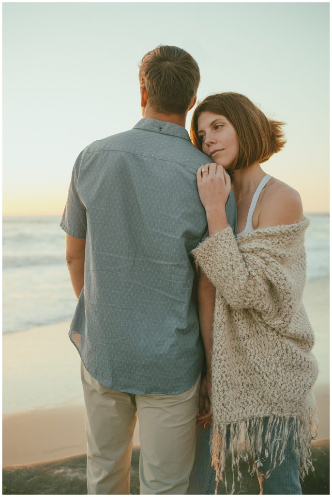 couple cuddling during golden hour engagement photo at beach engagement session location