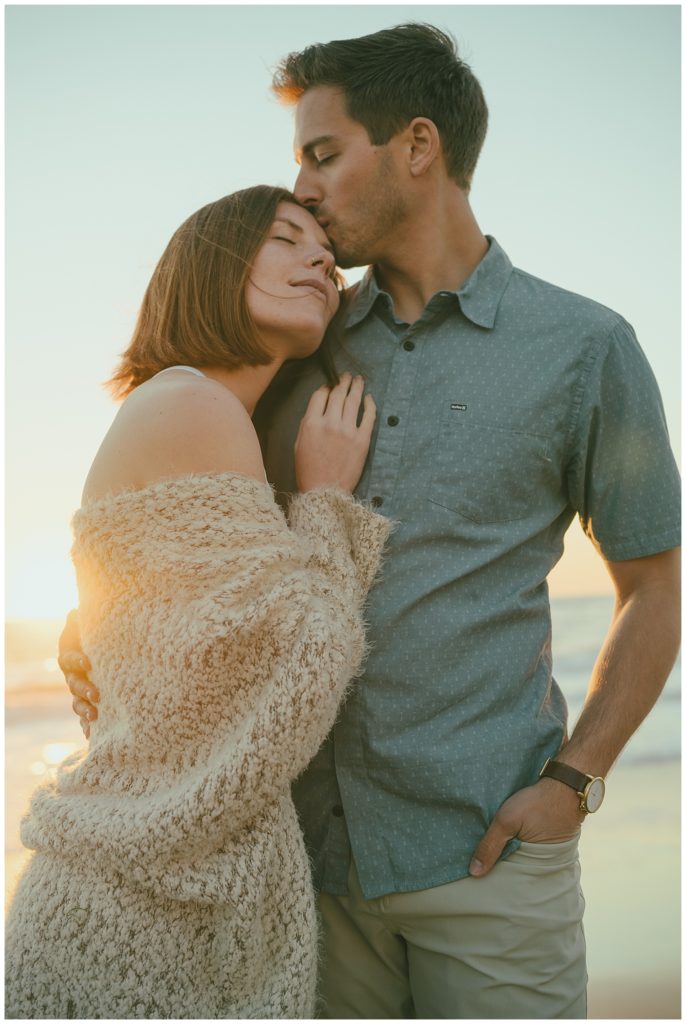 couple cuddling during golden hour engagement photo at beach engagement session location